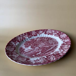 May include: An oval serving platter with a red and white floral and landscape design. The rim features a floral pattern, while the center showcases a detailed landscape scene. The platter is made of ceramic.