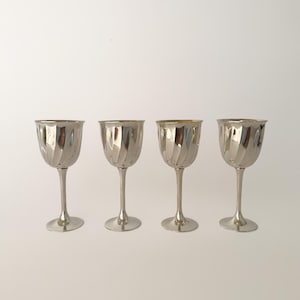 Op de afbeelding: Een set van vier zilverkleurige metalen bekers, elk met een gepolijste afwerking en een opvallend verticaal spiraal- of ribbelpatroon op de kelk. De bekers hebben een slanke steel en een ronde voet en staan in een rij opgesteld.
