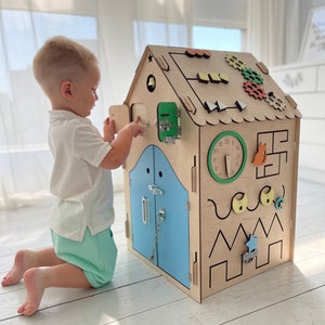 Puede incluir: Una casa de juegos de madera con una puerta azul, una esfera de reloj y varias otras actividades para que los ni&ntilde;os interact&uacute;en. La casa de juegos est&aacute; hecha de madera natural y tiene un acabado marr&oacute;n claro.