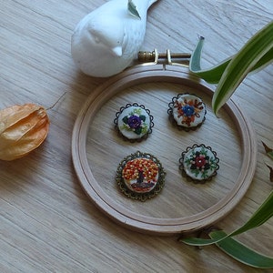Peut inclure: Quatre broches brodées dans un cercle à broder en bois. Les broches présentent une variété de motifs floraux et d'arbres avec des perles colorées et du fil à broder.