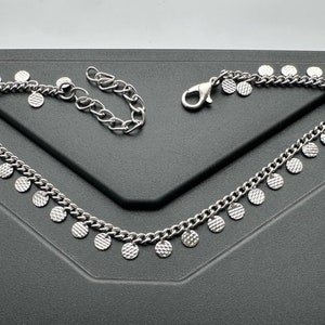 May include: A silver chain bracelet with a delicate design featuring small, round, textured charms. The bracelet has a lobster clasp closure.