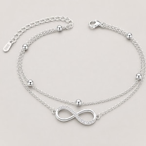 May include: A silver-coloured double-strand anklet. The anklet features small, round beads and a sparkling infinity symbol. The adjustable chain has a lobster clasp closure. The metal is stamped with "S925".