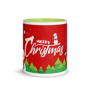 May include: A ceramic mug with a red exterior featuring a "Merry Christmas" design in white script. The design includes a snowman, Santa hat, and green Christmas trees. The interior of the mug is light green.