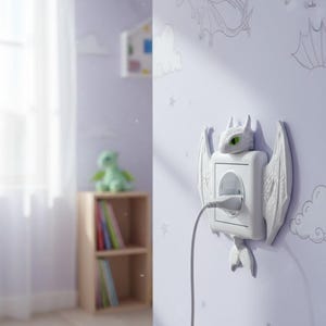 May include: A white dragon-themed electrical outlet cover with a charging cable plugged in. The dragon has green eyes and wings. The outlet is mounted on a light purple wall with dragon and star decals. The room has a wooden shelf and a green stuffed dragon.