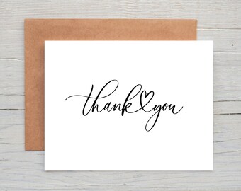 Puede incluir: Una tarjeta blanca con una fuente negra cursiva que dice "Gracias" con un pequeño símbolo de corazón en el medio de la palabra "Gracias".