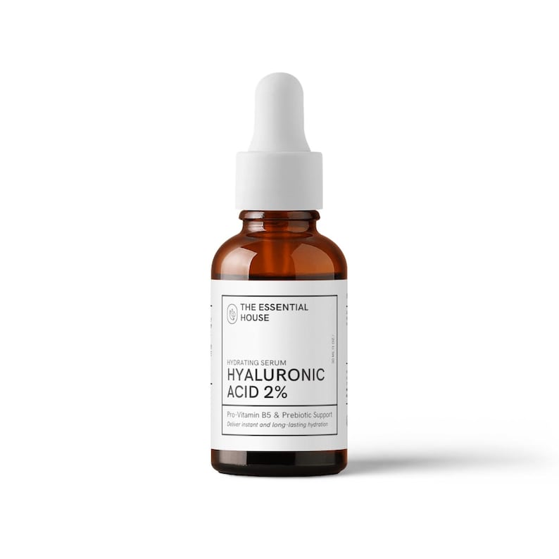Puede incluir: Una botella de vidrio marr&oacute;n de suero hidratante con un cuentagotas blanco. La etiqueta dice "THE ESSENTIAL HOUSE HYALURONIC ACID 2%" con texto sobre Pro-Vitamina B5 y soporte prebi&oacute;tico. La botella est&aacute; sobre un fondo blanco.
