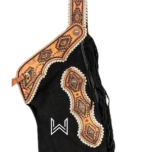 May include: Black leather chaps with decorative tan leather accents and fringe. The tan leather features geometric patterns and white stitching. A white "W" logo is visible on the left leg.