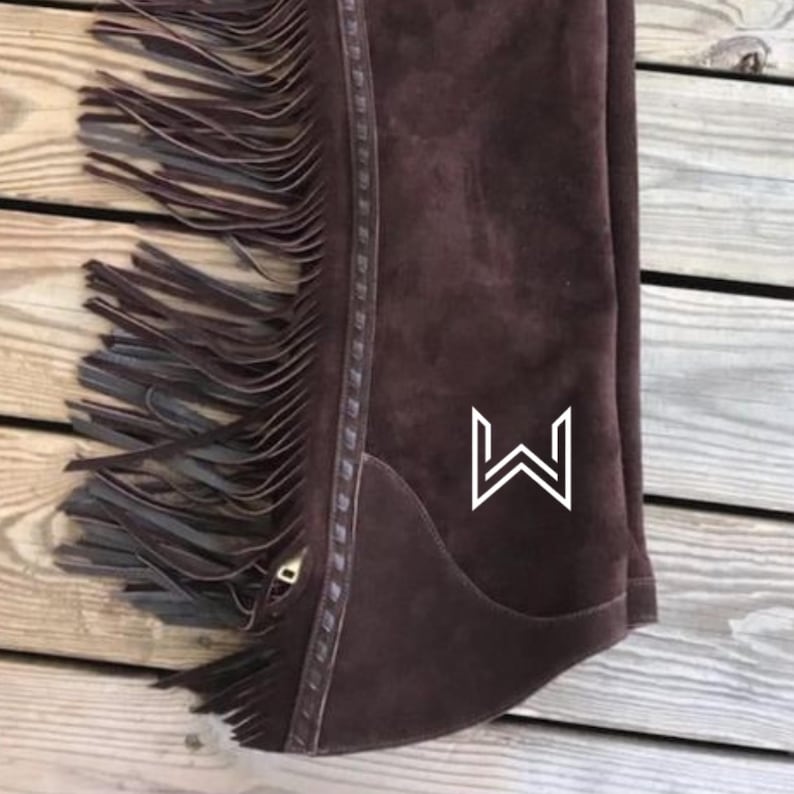 Pu&ograve; includere: Chaps da equitazione in pelle scamosciata marrone con dettagli a frangia e un logo "W" bianco.