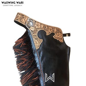Puede incluir: Chaps de cuero negro con un dise&ntilde;o floral decorativo en la parte superior y flecos en el lateral. La parte superior presenta cuero marr&oacute;n claro con patrones florales tallados y un emblema plateado. La marca "WAXWING WARI" est&aacute; en la parte superior.