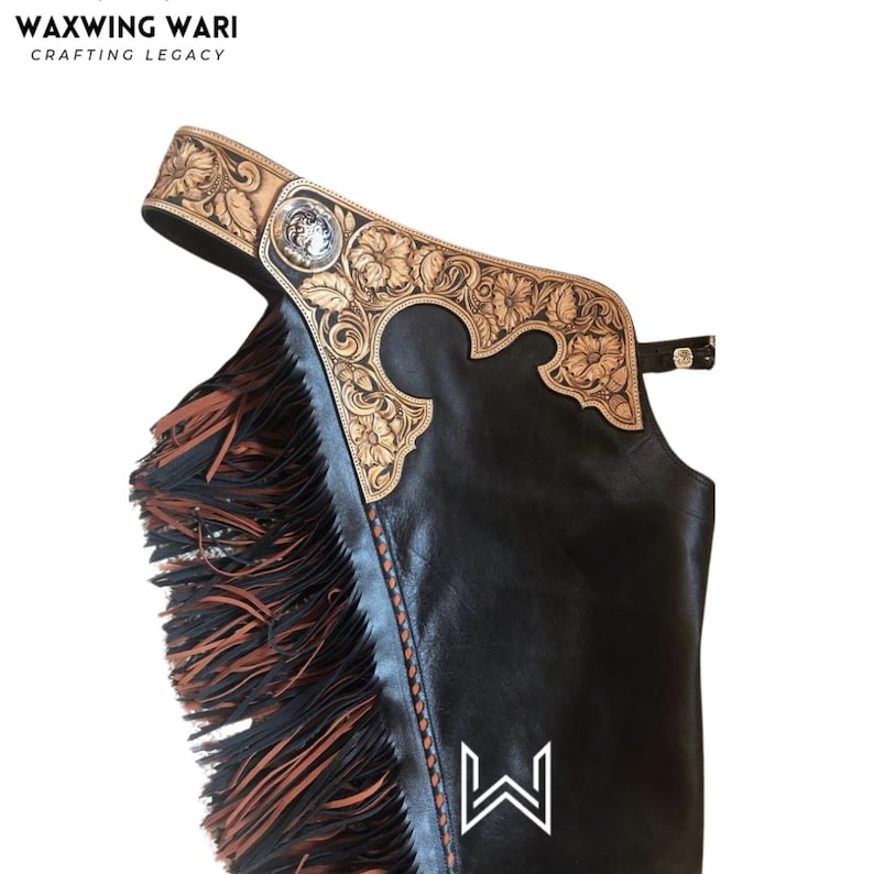 Puede incluir: Chaps de cuero negro con un dise&ntilde;o floral decorativo en la parte superior y flecos en el lateral. La parte superior presenta cuero marr&oacute;n claro con patrones florales tallados y un emblema plateado. La marca "WAXWING WARI" est&aacute; en la parte superior.