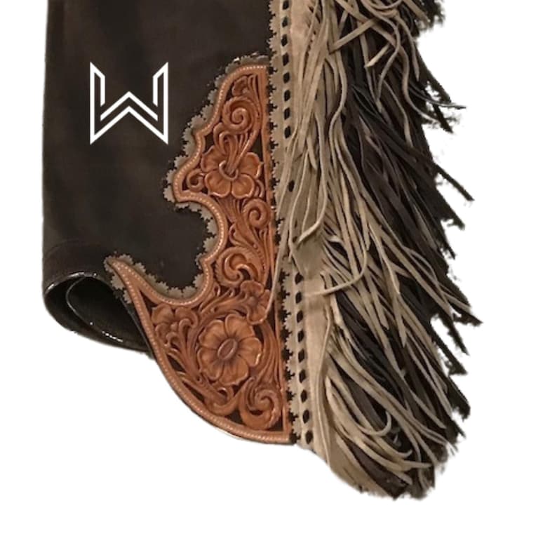 Puede incluir: Chaps de cuero marr&oacute;n con un dise&ntilde;o tallado y flecos. Los chaps tienen un logotipo "W" blanco en la parte delantera.