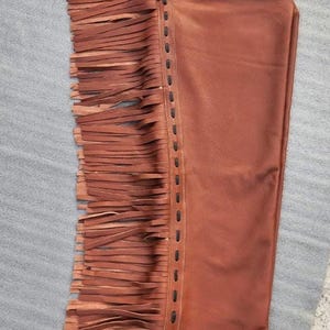 Pu&ograve; includere: Chaps in pelle marrone con frange decorative sul lato. Gli chaps presentano una cintura dettagliata con una fibbia color oro e cuciture decorative. La pelle &egrave; di un ricco e caldo colore marrone e le frange aggiungono un tocco di stile.