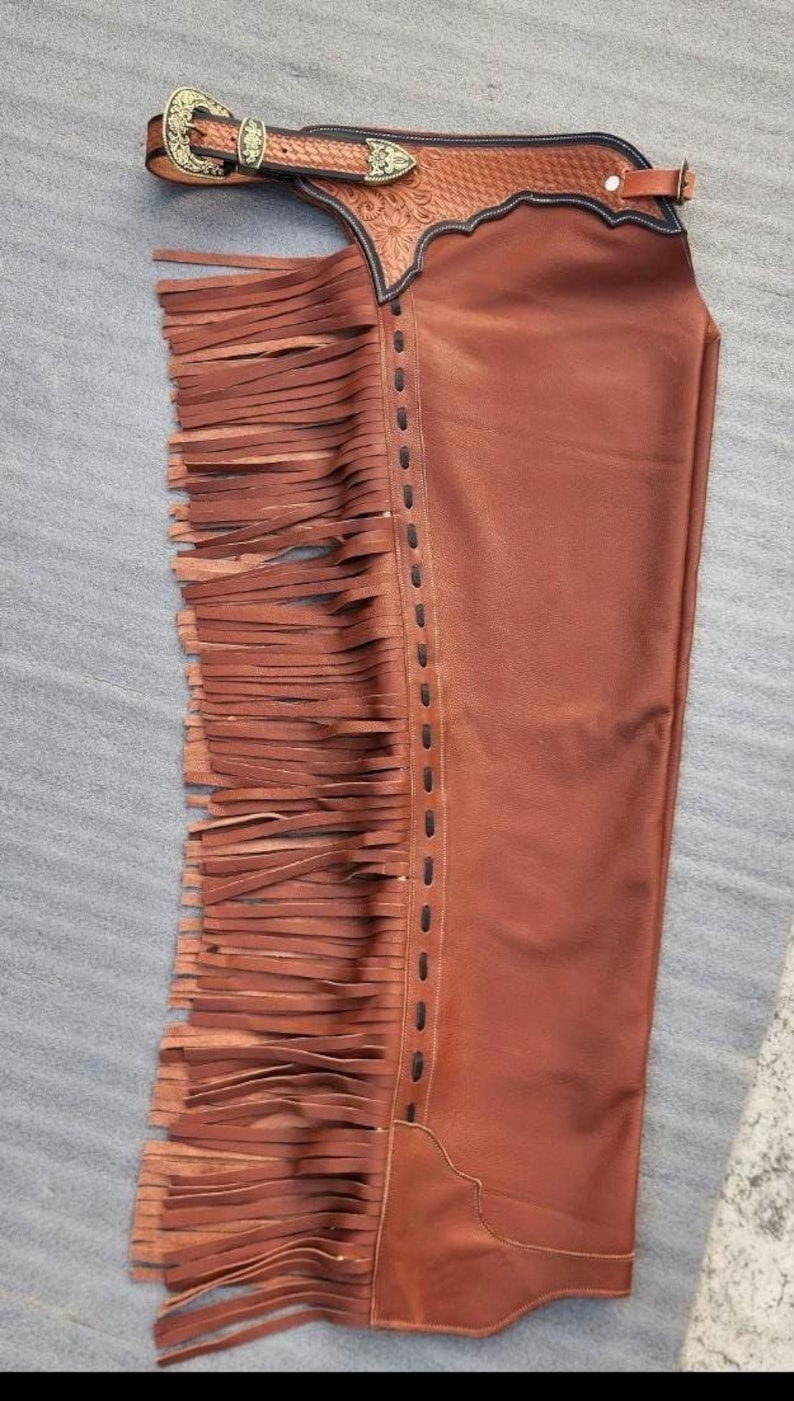Pu&ograve; includere: Chaps in pelle marrone con frange decorative sul lato. Gli chaps presentano una cintura dettagliata con una fibbia color oro e cuciture decorative. La pelle &egrave; di un ricco e caldo colore marrone e le frange aggiungono un tocco di stile.