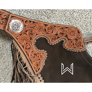 Puede incluir: Chaps de cuero marr&oacute;n con intrincados detalles florales y flecos. Los chaps tienen un concho plateado en el bucle del cintur&oacute;n y un logotipo "W" blanco en la parte posterior.