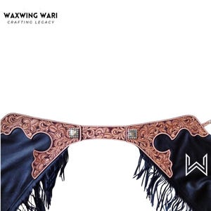 May include: Black leather chaps with intricate floral tooling in shades of brown and tan. The chaps feature a decorative yoke with silver-toned square accents and fringe along the bottom edge. The brand name "WAXWING WARI" is at the top.