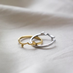 Puede incluir: Dos anillos entrelazados, uno dorado y otro plateado. El anillo dorado presenta un diseño de letra árabe estilizado.