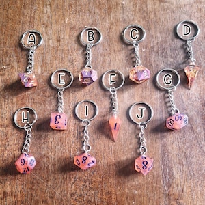 May include: Ten resin dice keychains in various shapes and colours. The dice are translucent and have black numbers. The keychains are attached to silver key rings.