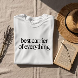 White t-shirt with "best carrier of everything" text, straw hat, and lavender.