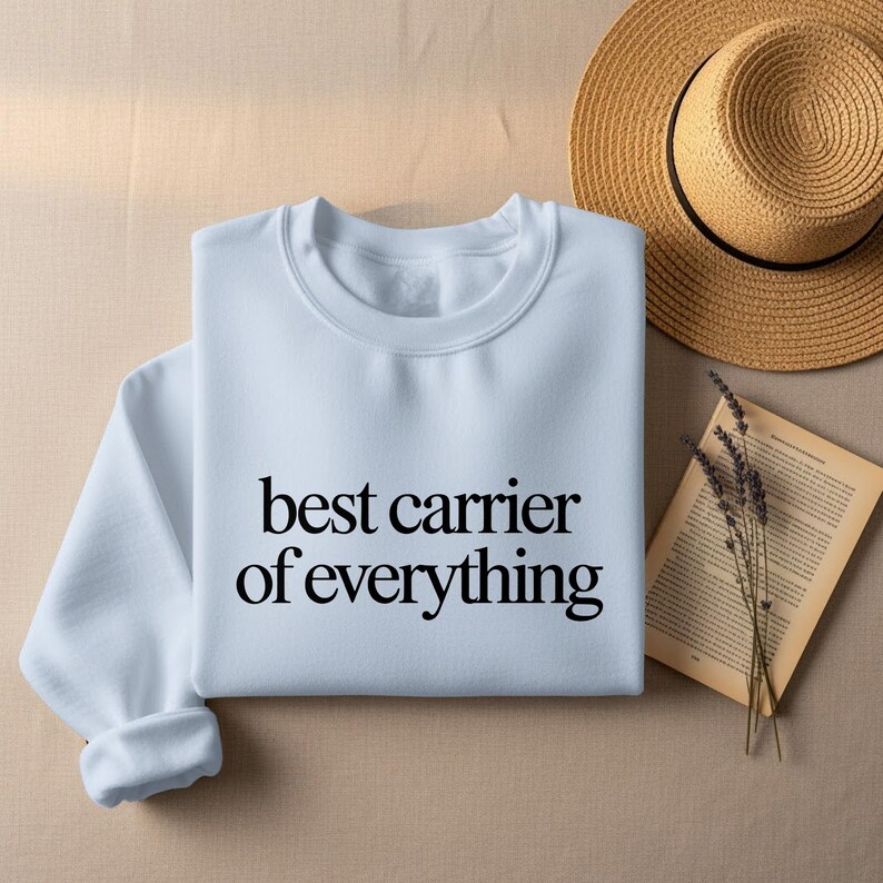 White sweatshirt with "best carrier of everything" text, hat and book.