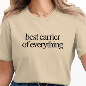 Beige t-shirt with "best carrier of everything" text.