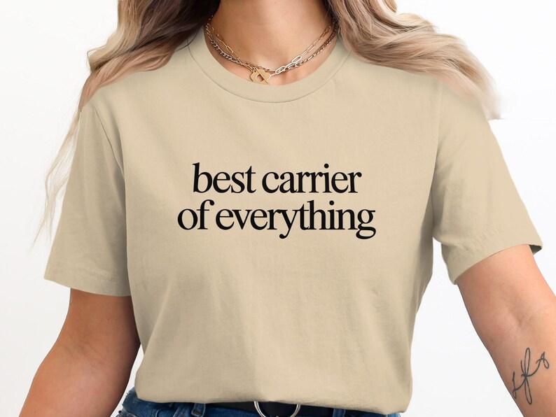 Beige t-shirt with "best carrier of everything" text.