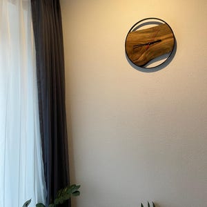May include: A wooden clock with a black metal frame and a wood grain design. The clock is hanging on a white wall.
