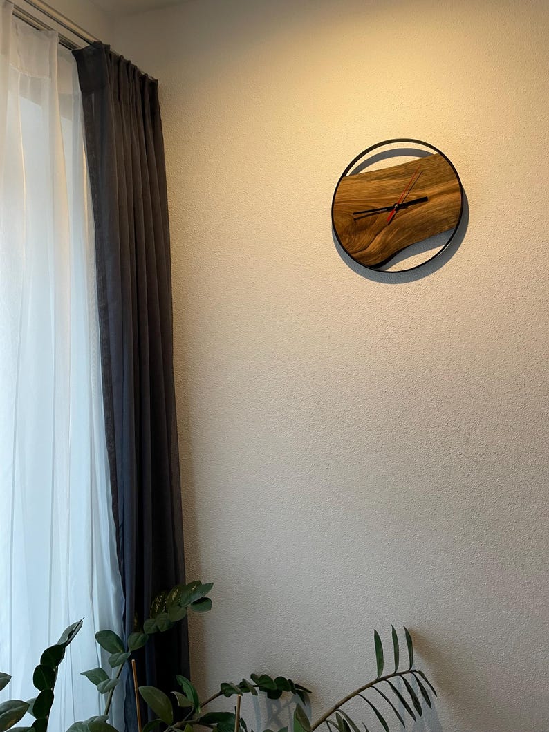 May include: A wooden clock with a black metal frame and a wood grain design. The clock is hanging on a white wall.