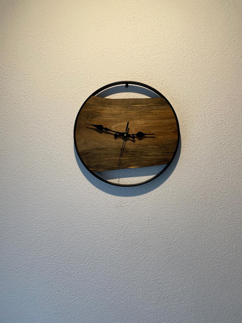 May include: A round wooden clock with black hands and a black metal frame. The clock is mounted on a white wall.