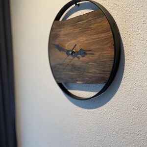 May include: A round wooden clock with black metal hands and a black metal frame. The clock face is made of dark wood with a natural grain pattern.
