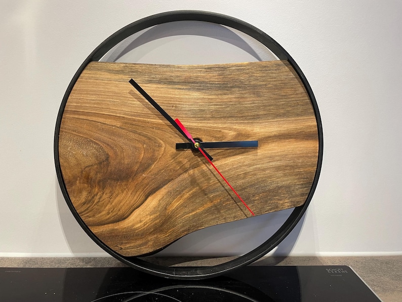 May include: A wooden clock with a black metal frame. The clock face is made of a dark wood with a natural grain pattern. The clock hands are black and red.