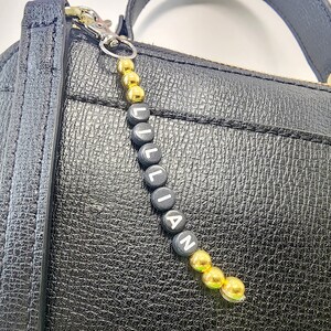 May include: A black leather handbag with a gold and black beaded keychain that spells "LILLIAN".