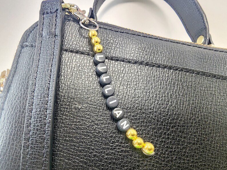 May include: A black leather handbag with a gold and black beaded keychain that spells "LILLIAN".