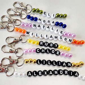May include: A set of eight beaded keychains with different names spelled out in black letters. The beads are various colors, including green, blue, orange, yellow, pink, and white.