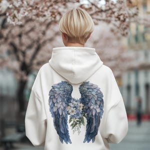 May include: White hoodie with a blue and purple watercolor angel wings design on the back. The wings are surrounded by white flowers.