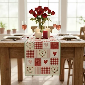 May include: A wooden dining table set for a romantic occasion. A red and white heart-patterned table runner is centered, complemented by red roses in a vase, candles, and wine glasses. Plates and silverware are set for a meal.