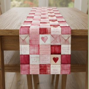 May include: A Valentine's Day themed table runner with a patchwork design. The runner features squares in shades of red and pink, with heart and envelope motifs. Handwritten script adds a vintage touch to the design. The runner is displayed on a wooden table.