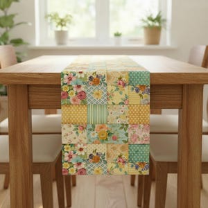 Op de afbeelding: Een patchwork tafelloper met bloemen- en geometrische patronen in pasteltinten geel, roze en blauw. De loper wordt getoond op een houten tafel. Het ontwerp van de loper omvat stippen, strepen en bloemenprints.