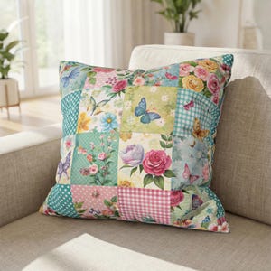 May include: Square decorative pillow with a patchwork design. The pillow features squares with floral and butterfly patterns in shades of pink, green, blue, and yellow. The pillow is resting on a beige sofa.