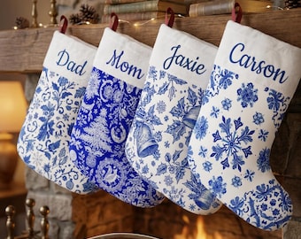 Op de afbeelding: Vier kerstsokken met witte boorden en blauw-witte patronen. De boorden zijn geborduurd met de namen Dad, Mom, Jaxie en Carson in blauw schrift. De sokken zijn voorzien van diverse ontwerpen, waaronder bloemmotieven, bomen en klokken.