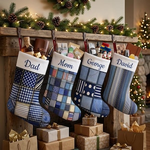 May include: Four Christmas stockings hanging from a wooden mantel, each featuring a white cuff with embroidered names Dad, Mom, George, and David. The stockings are crafted from various blue fabric patches, including plaid, polka dot, and striped patterns.