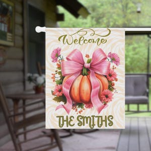 Peut inclure: Un drapeau de jardin décoratif avec une citrouille ornée d'un grand nœud rose et de fleurs. Le drapeau affiche le mot "Welcome" et "THE SMITHS" sur un fond crème à motif zébré.