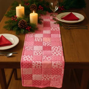 May include: A rectangular table runner featuring a patchwork design composed of various pink fabric squares. The fabric patterns include polka dots, floral prints, and geometric lines, all in shades of light and dark pink, stitched together in a grid.