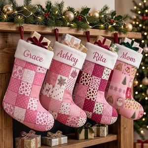 May include: Four personalized Christmas stockings hanging in a row, each featuring a white cuff with names Grace, Ashley, Rita, and Mom embroidered in pink. The stockings are made of pink and white patchwork fabric with various patterns and prints.