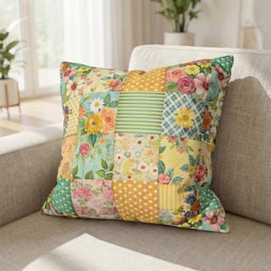 May include: Square decorative pillow with a patchwork design. The pillow features various floral patterns, including roses and daisies, in shades of yellow, pink, and blue. The pillow is placed on a neutral-colored sofa.