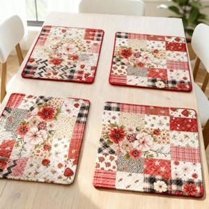 Puede incluir: Cuatro manteles individuales cuadrados acolchados con un diseño de patchwork. Cada mantel presenta un estampado floral con flores rojas, rosas y crema, fresas y varios patrones geométricos. Los manteles tienen un borde rojo y están colocados sobre una mesa de madera clara.