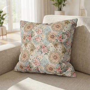 May include: Square cushion with a floral patchwork design. The cushion features a pattern of pink roses, tan flowers, and light blue squares. The cushion is placed on a beige sofa.