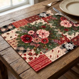 Puede incluir: Un mantel individual acolchado rectangular con un diseño de patchwork de cuadrados de tela a cuadros rojos, blancos y negros, rojo sólido y color crema. El centro muestra un estampado de ramas de pino, piñas y flores rojas.
