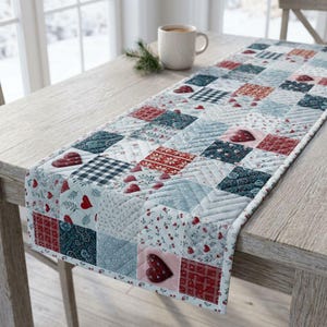 May include: A quilted table runner featuring a patchwork design of squares in shades of red, white, and blue. The fabric squares display various patterns including small hearts, floral motifs, plaid, and geometric prints with visible stitching.