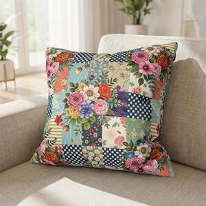 May include: Square cushion with a patchwork design featuring floral patterns and various textures. The cushion has a mix of colours, including pink, orange, blue, and green, with a white background. The cushion is placed on a beige sofa.