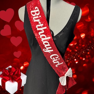 May include: Red sequined sash with white text that reads "Birthday Girl". The sash has a white bow on the end.